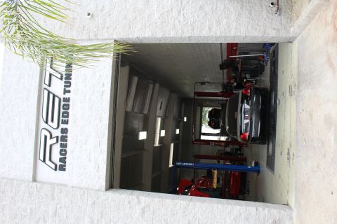 2003 Ford Crown Victoria - Exterior view through a shop bay door labeled Racers Edge Tuning with a black sedan on a dyno inside.
