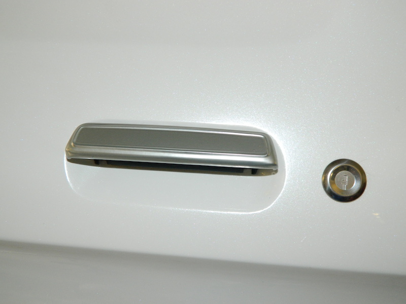 Close-up of a white vehicle's door handle and lock cylinder