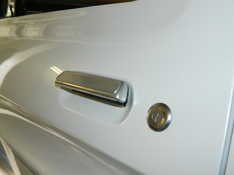 Close-up of a chrome door handle and lock cylinder on a white vehicle door