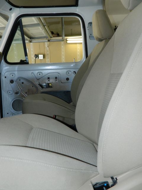 1979 Ford Bronco - The interior of a vehicle shows light-colored seats and the exposed door frame, with a garage visible through the open window.