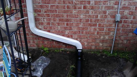 1994 Ford Bronco - A white downspout directs water from a gutter down to a black drain pipe against a red brick wall.