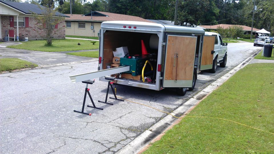 1994 Ford Bronco towing an open trailer with equipment, including a long metal beam on sawhorses