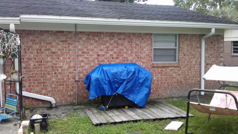 1994 Ford Bronco - A grill is covered by a blue tarp on a wooden platform in front of a brick house.