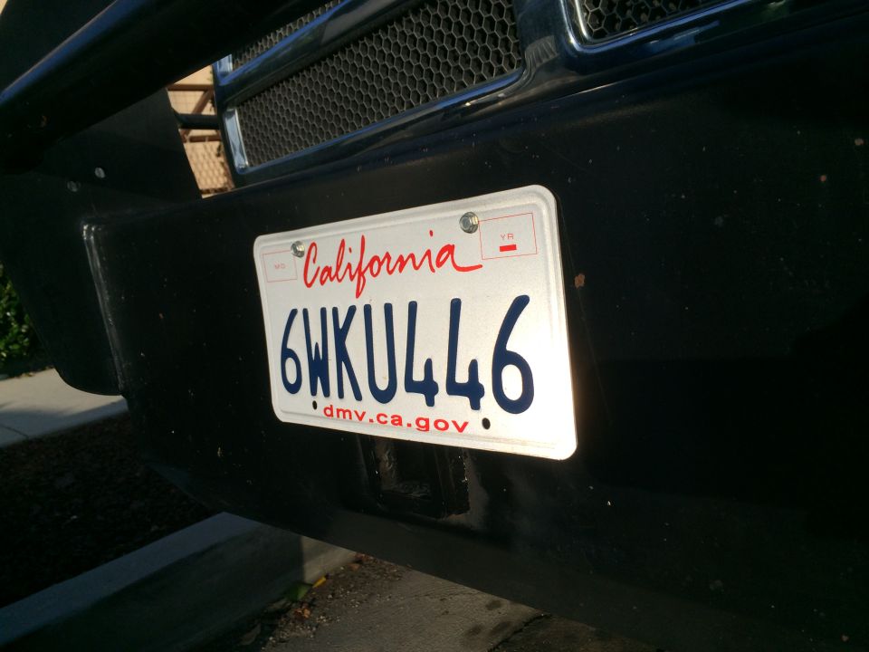 California license plate 6WKU446 mounted on a black bumper, with a grille visible above