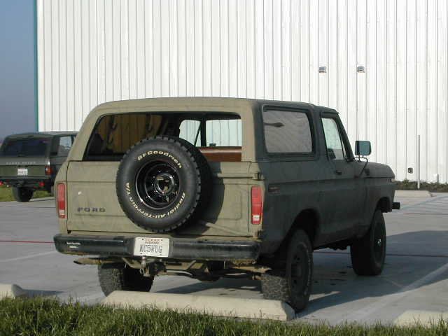 Tan 1978 Ford Bronco with spare tire on rear, parked next to a dark green SUV