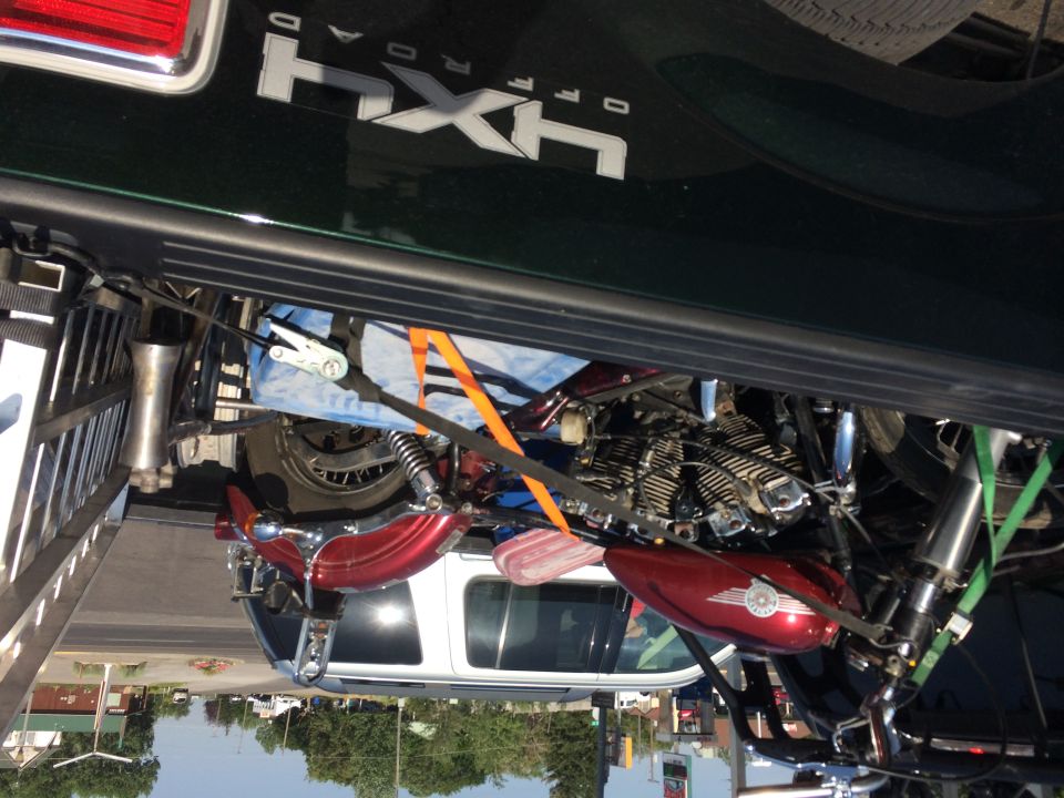 Red Harley motorcycle tied down in the bed of a green 4x4 pickup, photo rotated sideways