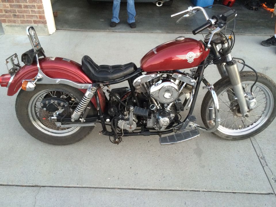 Right side of a red Harley-Davidson Shovelhead motorcycle with solo seat and sissy bar on a driveway