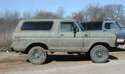 1978 Ford Bronco - This 1978 Ford Bronco, painted in a camouflage pattern, is seen parked outdoors next to another truck.