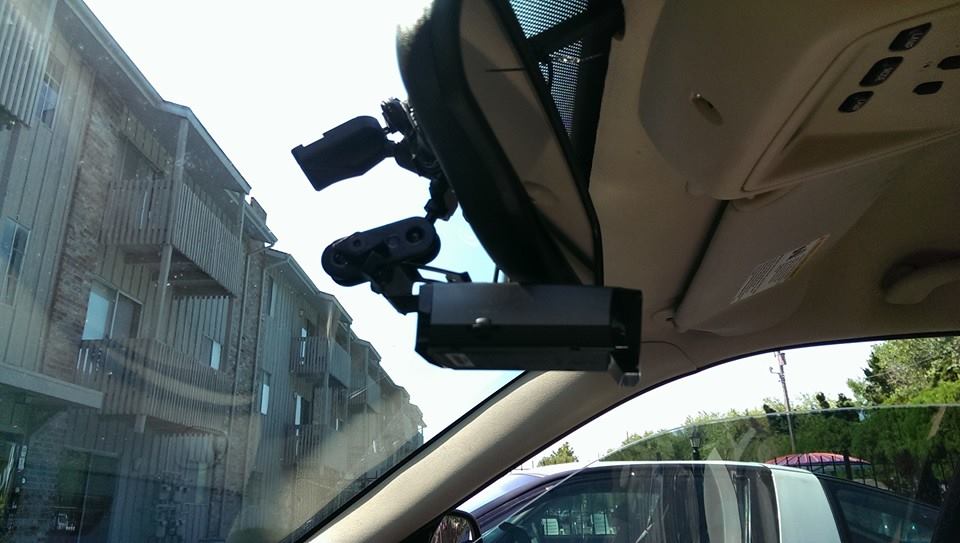 Dashcam and radar detector mounted on windshield, apartment buildings outside
