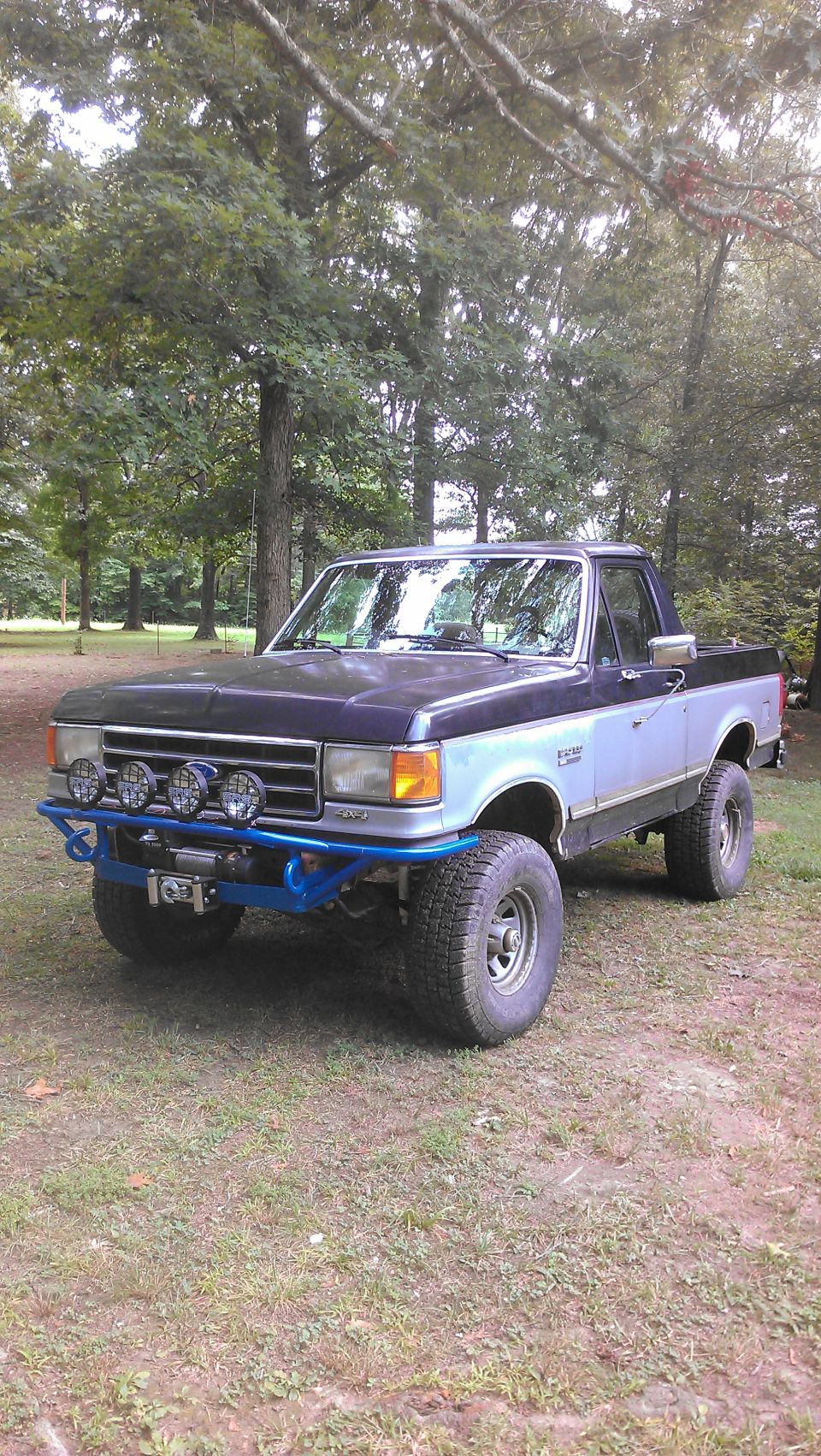 Blue and silver Ford F-Series truck with aftermarket bumper and lights, parked on grass