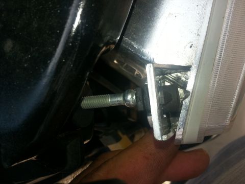 1994 Ford Bronco - Close-up of a headlight mounting bolt being removed from a vehicle's assembly.