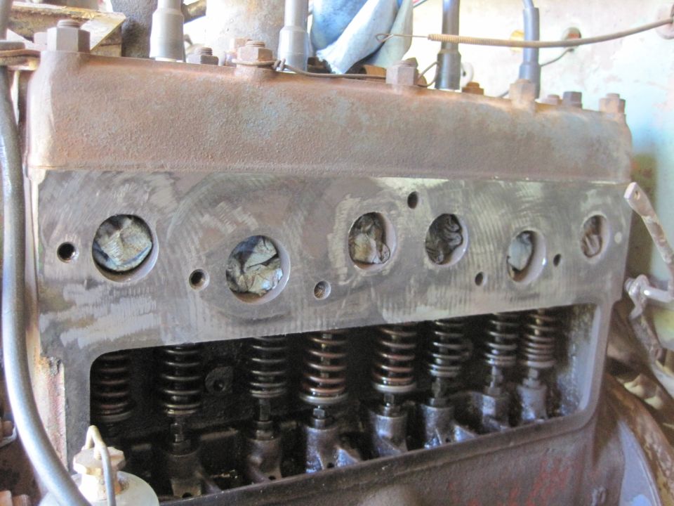 Close-up of an old engine's cylinder head with valves and springs visible. Some cylinders are covered with cloth