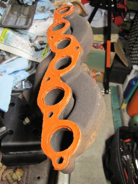 1946 Jeep Willys - An exhaust manifold gasket, prepared with orange sealant, sits on a cluttered workbench.