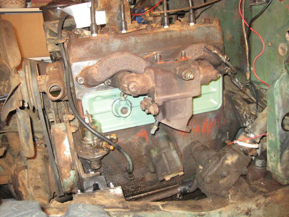 Engine block with carburetor, fuel pump, and spark plug wires. Some parts are rusty