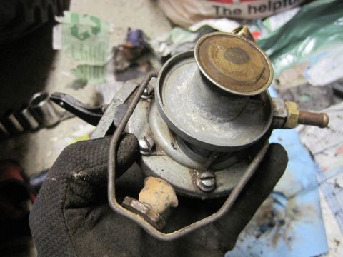 1946 Jeep Willys - A gloved hand holds a metal fuel pump, a component for a vehicle's engine.