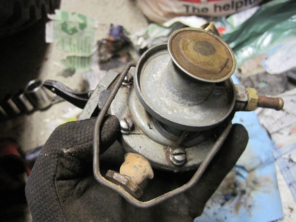 Gloved hand holds a metal fuel pump with a brass fitting and a circular top