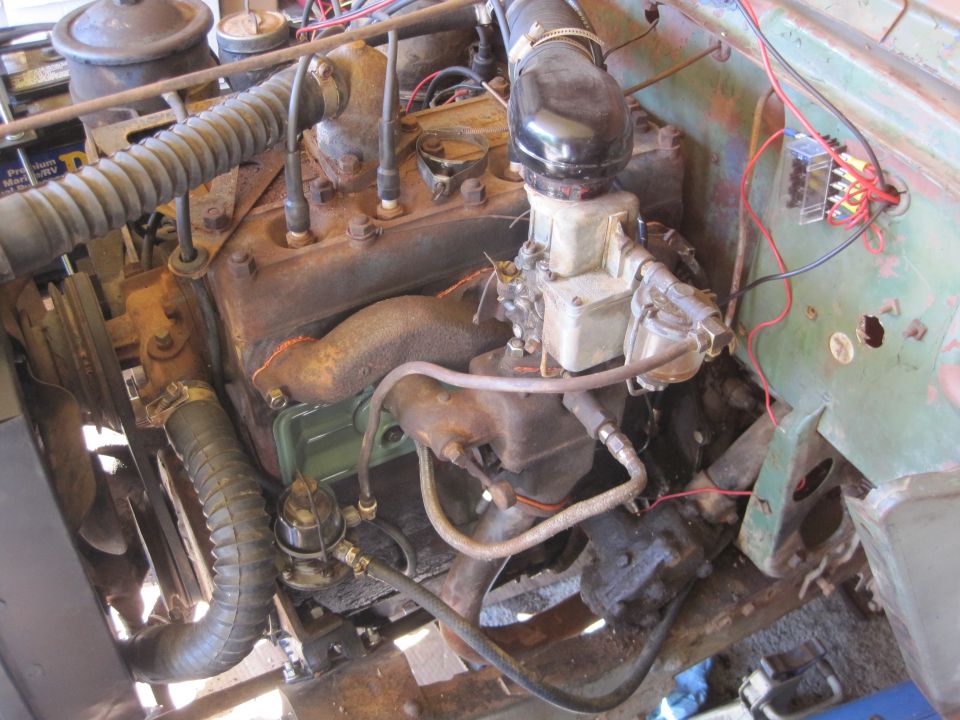 Close-up of a rusty Jeep engine with hoses, carburetor, and wiring visible