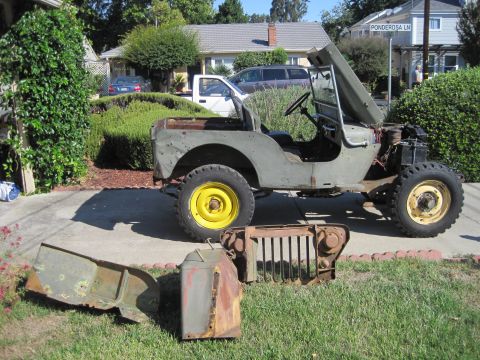 1946 Jeep Willys - Olive drab Jeep CJ5 with hood open and disassembled parts on the grass in front of a suburban house.