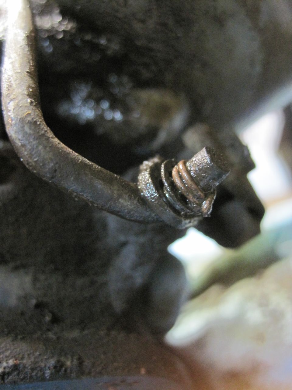 Close-up of a rusty metal hose clamp with a spring on a dark, greasy engine part