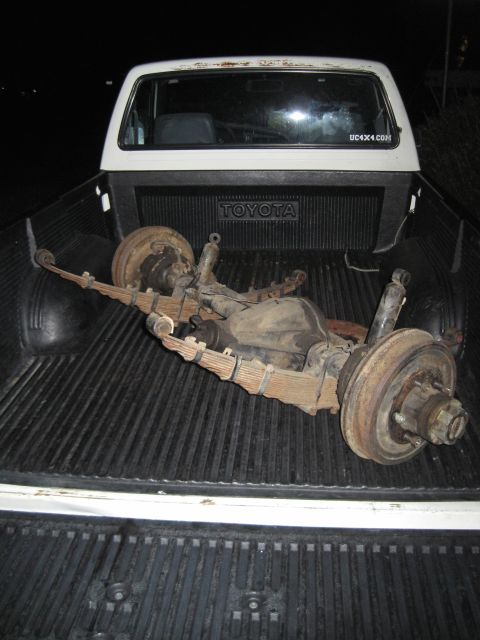 1946 Jeep Willys - An axle assembly with leaf springs and shocks is loaded into the bed of a white Toyota pickup truck.