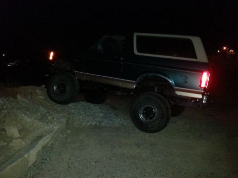 1996 Ford Bronco - A lifted Ford Bronco with off-road tires navigates rough terrain in the dark.