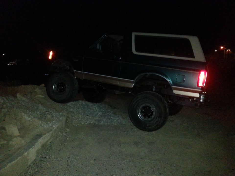Dark green Ford Bronco with a white top, lifted suspension, and off-road tires, viewed from the side at night