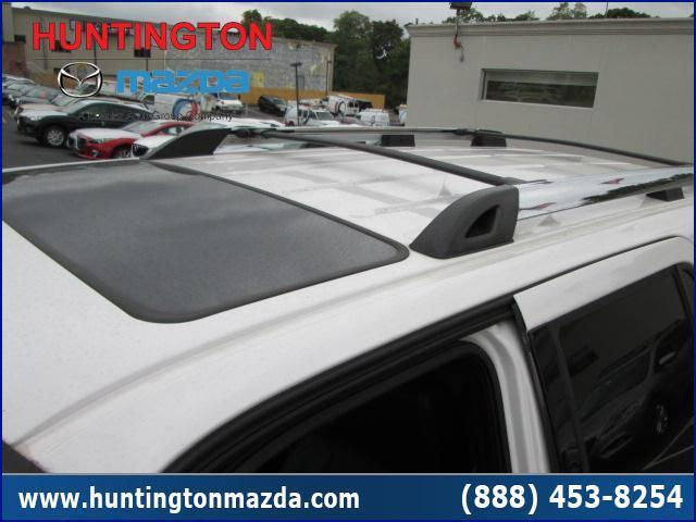 White SUV roof with sunroof and roof rack, parked in a lot with other vehicles