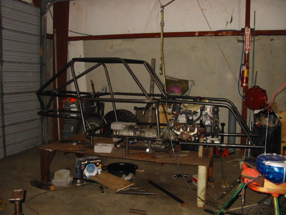 Bare tube-frame chassis with roll cage on a workbench in a shop
