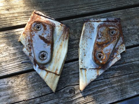 1964 Ford Fairlane - These two heavily rusted metal brackets, likely automotive parts, are shown resting on a weathered wooden surface.