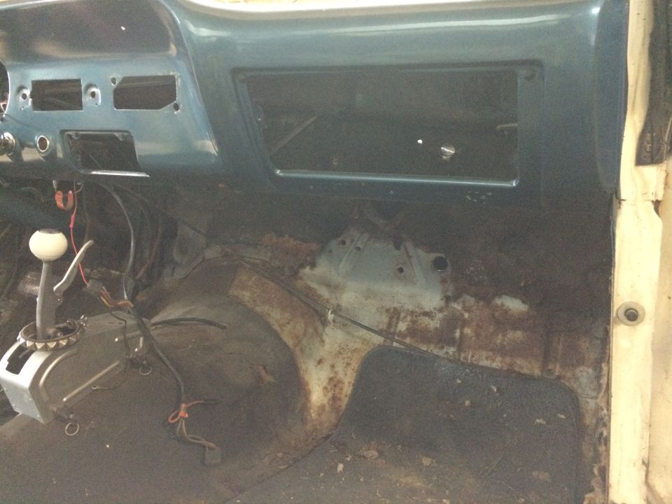 Interior of a car showing a rusted floor pan, an automatic transmission shifter with a white knob, and the dashboard area