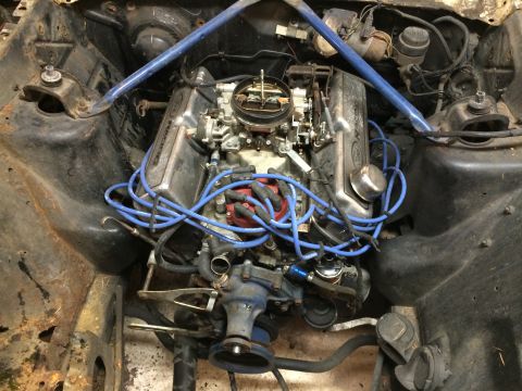 1964 Ford Fairlane - The engine bay of a vehicle, showing a V8 engine with prominent blue spark plug wires and a carburetor.