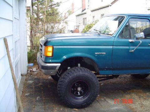 1989 Ford Bronco - A teal Ford Bronco with aftermarket wheels and suspension is parked outdoors.