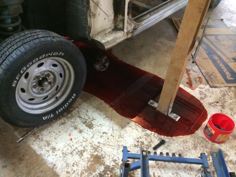 1964 Ford Fairlane - Car body with a tire and red fluid leaking onto the floor, with a wooden support in the spill.