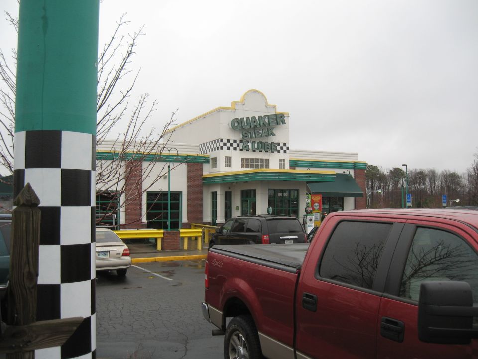Quaker Steak & Lube restaurant with checkered flag pole and vehicles in parking lot