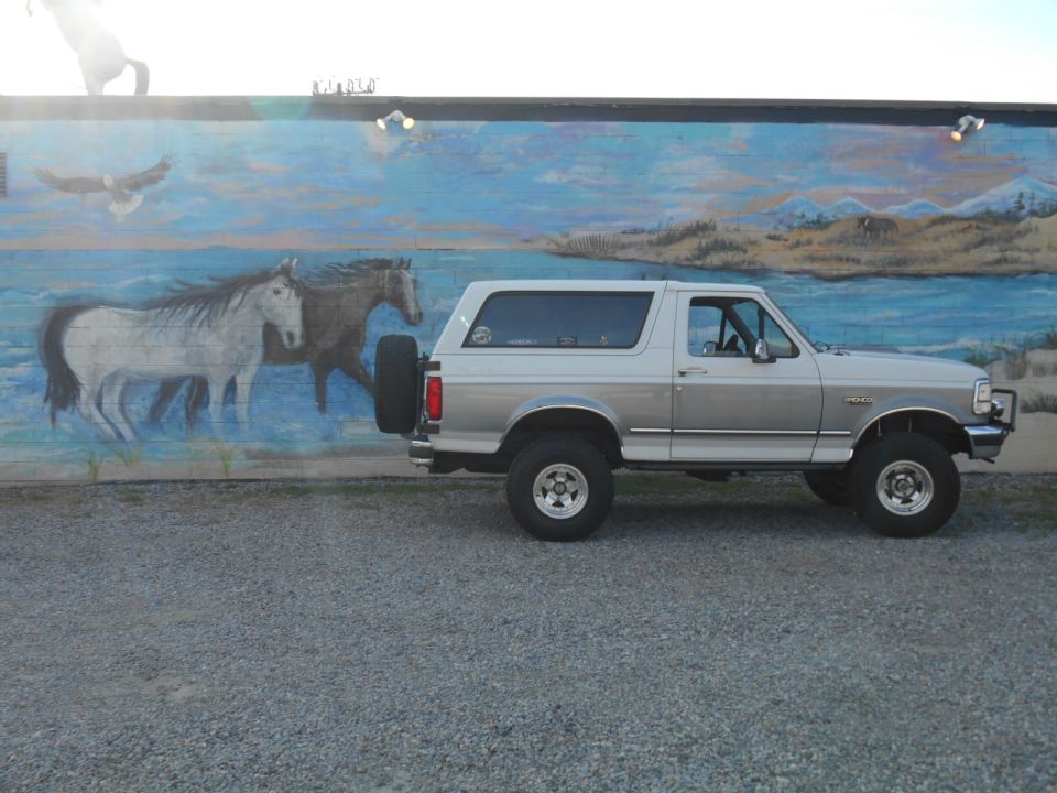 Side view of a 1994 Ford Bronco parked in front of a mural with horses and an eagle