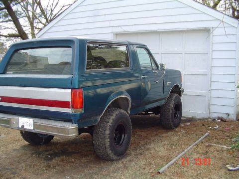 1989 Ford Bronco - 1989 Ford Bronco with aftermarket wheels and tires parked outside a garage.