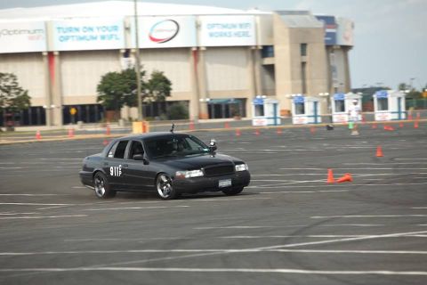1998 Ford Crown Victoria - Black sedan marked '911' running an autocross course laid out with cones in a large stadium parking lot.