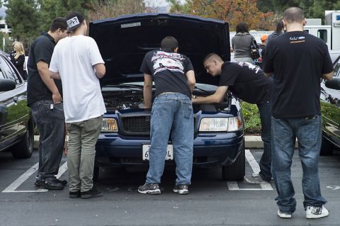 1998 Ford Crown Victoria - group of young men gather around the open hood of a blue pickup with a California plate in a parking-lot car meet.