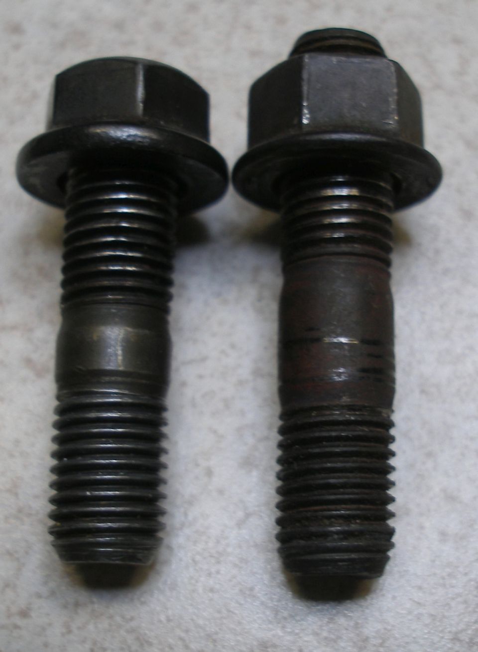 Two metal bolts with hex heads and integrated washers, one slightly rusted