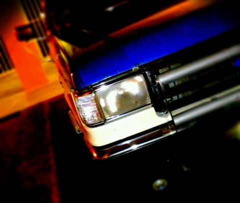 1990 Ford Bronco - Close-up of a blue and white Ford Bronco's front end, showing the grille and headlight assembly.