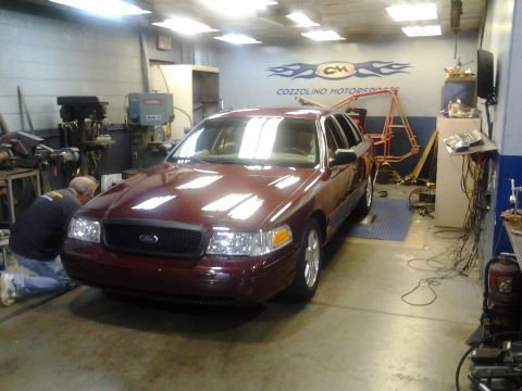 2004 Ford Crown Victoria - A maroon 2004 Ford Crown Victoria is in a garage, possibly being serviced, with a mechanic kneeling near the front bumper.