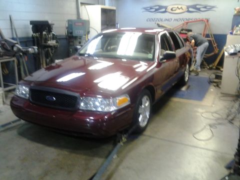 2004 Ford Crown Victoria - A maroon sedan is positioned on a lift inside a garage with tools and equipment visible.