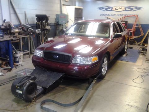 2004 Ford Crown Victoria - A maroon 2004 Ford Crown Victoria is positioned on a dynamometer in a workshop setting.