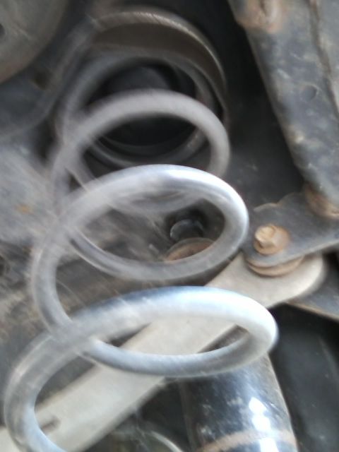 1999 Mercury Grand Marquis - A blurry close-up shows a suspension spring and associated metal parts of a vehicle's undercarriage.