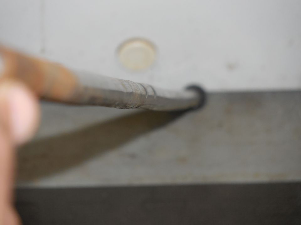 Close-up of a metal rod being held by a hand, with a circular hole in the background