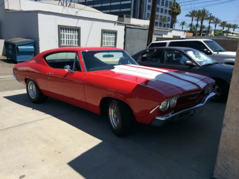 1968 Ford Mustang - A red 1969 coupe with white racing stripes is parked next to other vehicles.