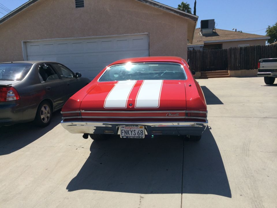 Red muscle car with white stripes on rear, parked next to a gray sedan