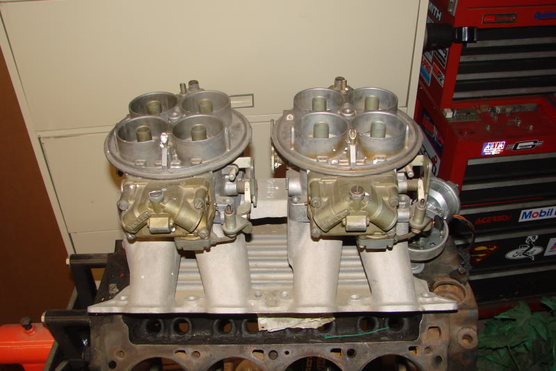 Dual carburetors mounted on an engine block, with a red toolbox in the background