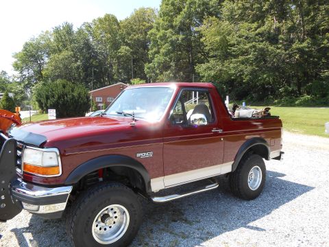 1992 Ford Bronco - A maroon 1992 Ford Bronco is parked outdoors, showing its side profile with a snow plow attachment on the front.