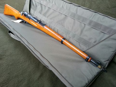 2003 Ford Crown Victoria - A rifle rests on a green padded gun case, its wooden stock gleaming.